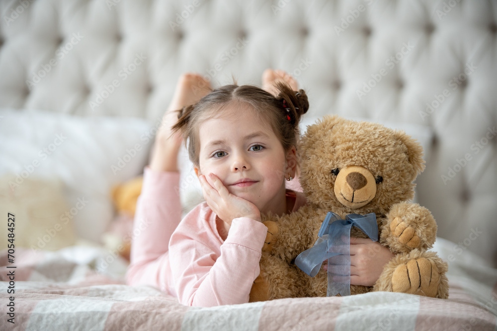 Cute little girl in pajama hugging her toy hare on the bed at home ...