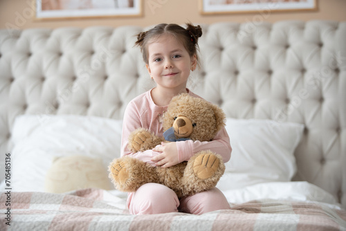 Cute little girl in pajama hugging her toy hare on the bed at home, happy childhood concept