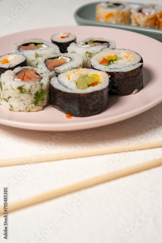 Chop sticks, mushrooms, noodle ramen, California rolls and Philadelphia rolls on a small plate on a pink background
