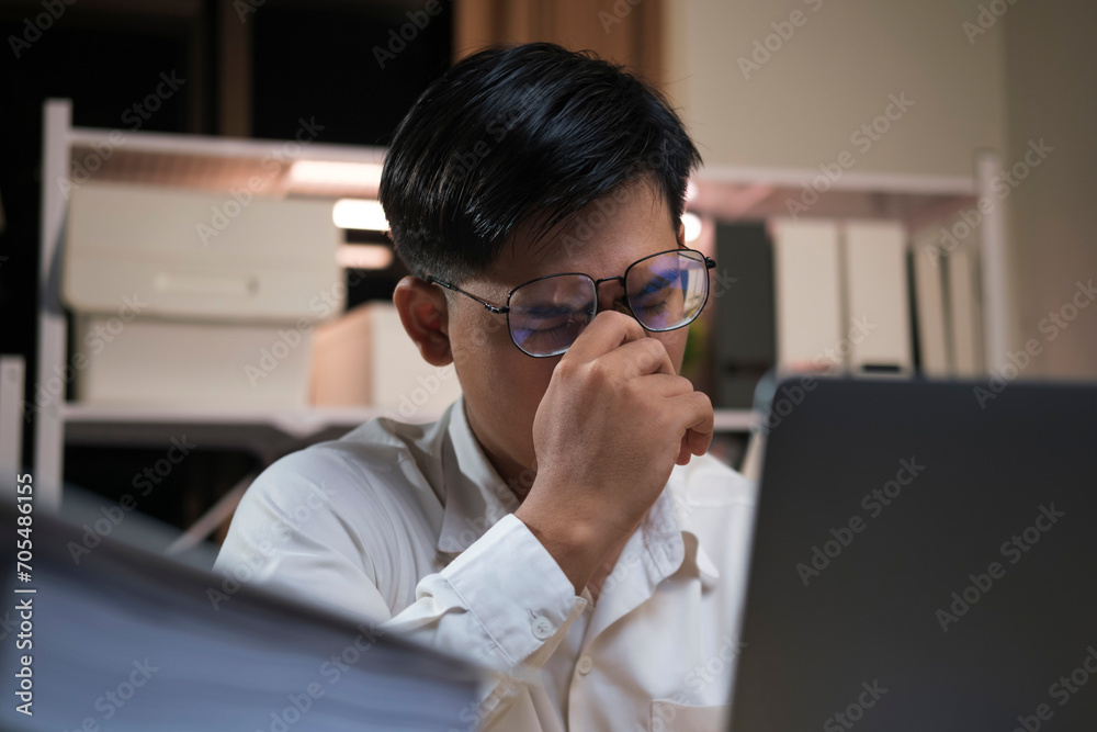 Exhausted young man with laptop in office.. Exhausted young man with laptop in office..
