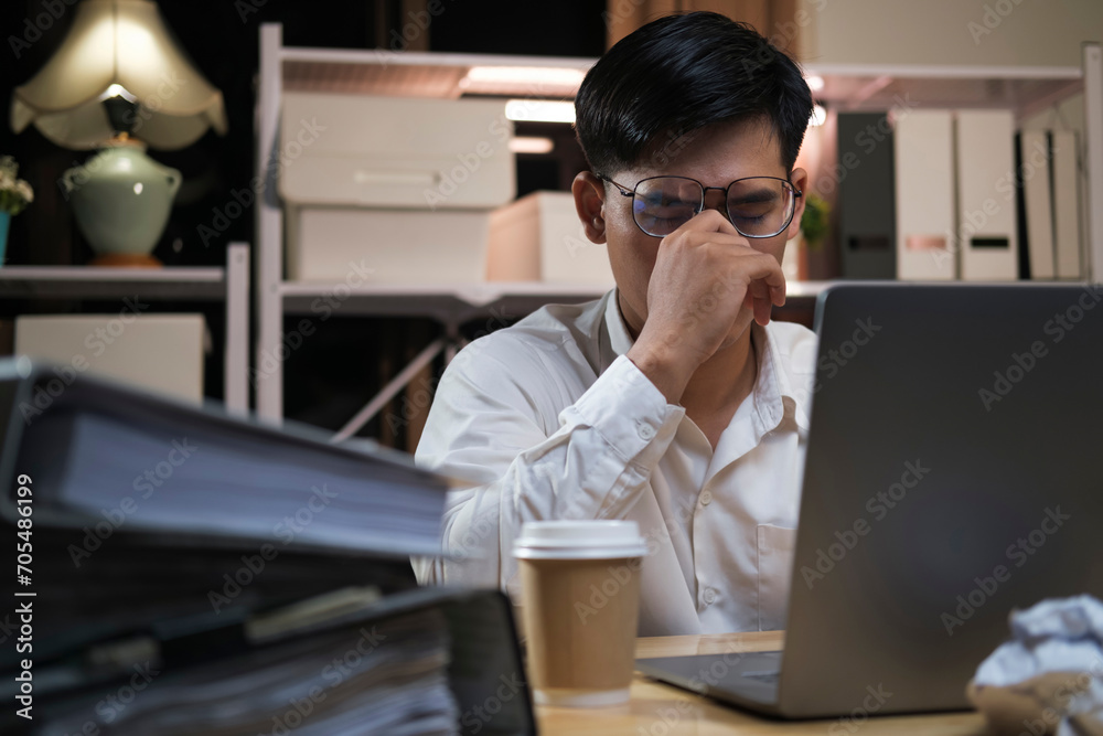 Exhausted young man with laptop in office.. Exhausted young man with laptop in office..
