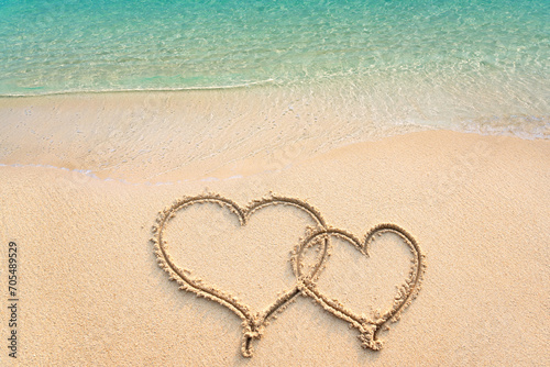 Two hearts handwritten on sandy beach with ocean wave on background. Two hearts drawn on sand with clear blue sea, copy space. Concept of luxury Honeymoon travel and greetings for valentine\'s day.