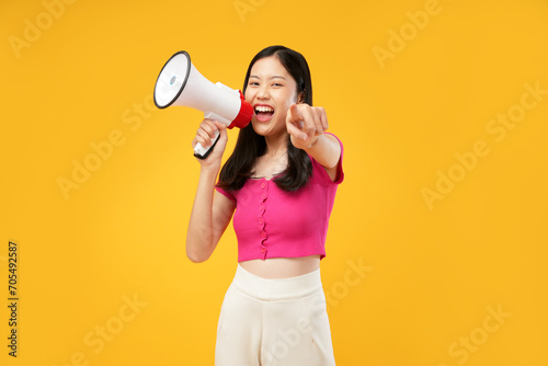 Photo of a young Asian woman wearing a pink t-shirt, holding a megaphone pointing forward, join us, or demonstration concept. Isolated on a yellow background.