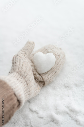Hand in beige mitten holding heart shaped snowball on white background