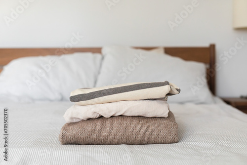 Minimalist style sweaters and shirts stacked on the bed © Cavan