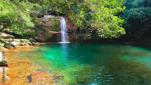 Jungle waterfall with white waters running down Rocky ridge of hill to blue green water of lagoon or pool. Sun rays passing through clear water. Rangshokham falls of Meghalaya. photo