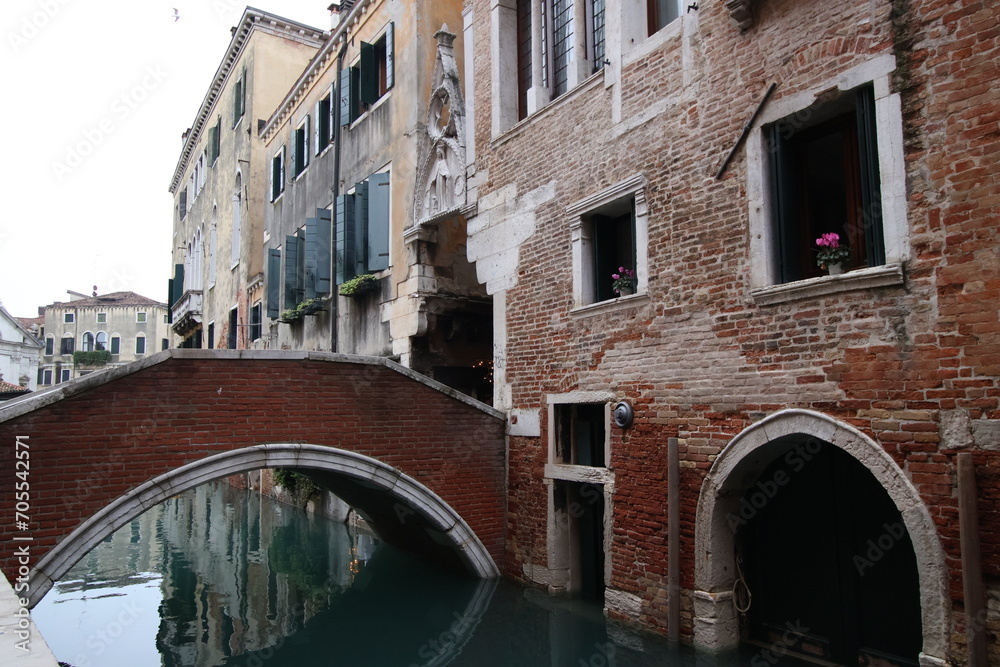 Picturesque bridge stretches across a tranquil body of water in front of an old building in Venice