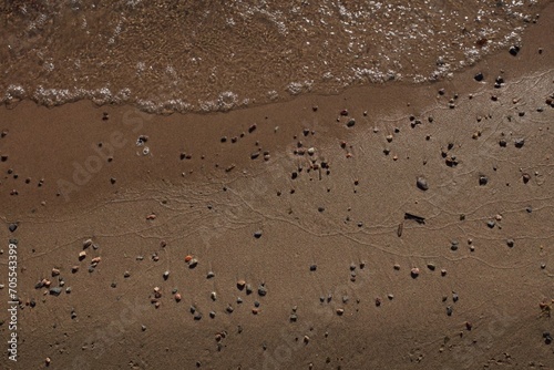 Top view of stones lying on a wet sand beach and sea water with bubbles.