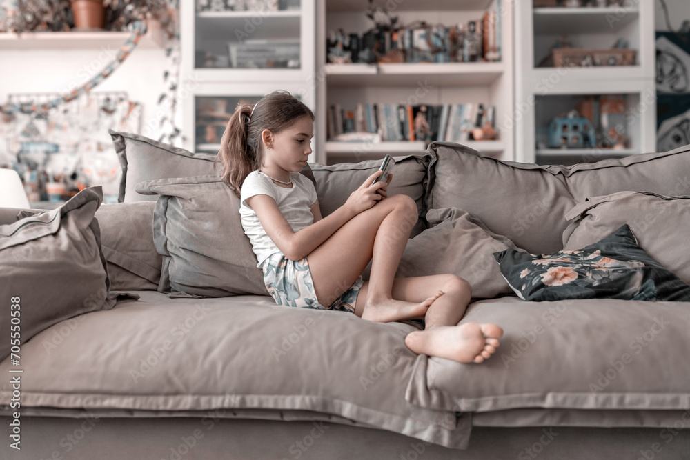Obraz premium Girl on mobile phone watching video on the couch at home; Suitable for smartphone, boredom, stay at home concept