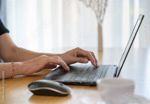 Woman using laptop computer while typing on her notebook while working online from home. 
