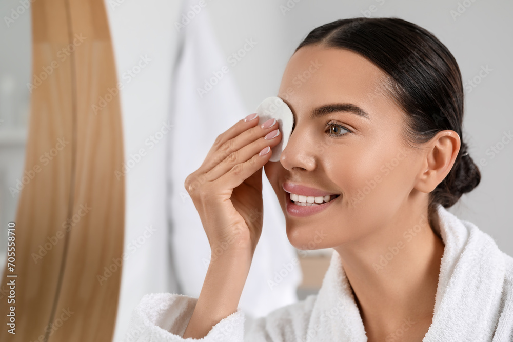 Beautiful woman removing makeup with cotton pad near mirror indoors Beautiful woman removing makeup with cotton pad near mirror indoors