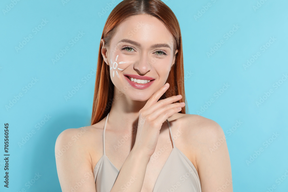 Fototapeta premium Beautiful young woman with sun protection cream on her face against light blue background