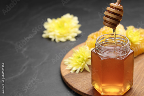 Pouring sweet honey from dipper into jar at grey table  space for text
