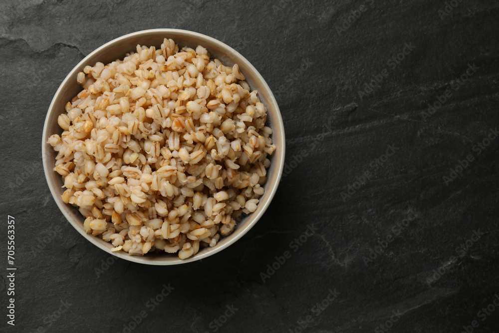 Tasty pearl barley porridge in bowl on dark textured table, top view. Space for text