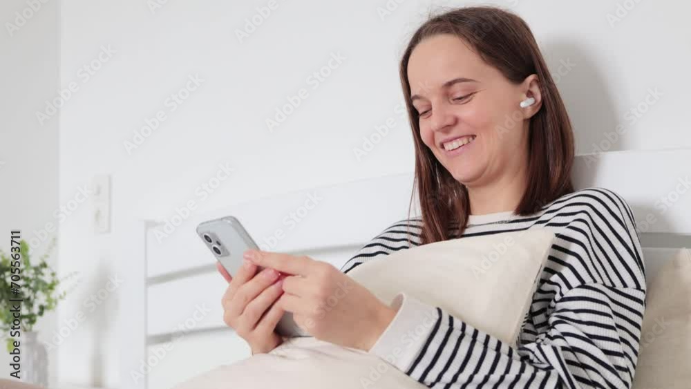 Cheerful happy positive attractive young adult woman wearing casual clothing holding smartphone in hands watching funny video in internet laughing sincerely Cheerful happy positive attractive young adult woman wearing casual clothing holding smartphone in hands watching funny video in internet laughing sincerely