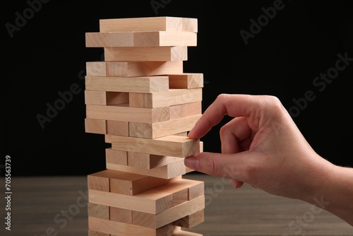 Woman playing Jenga at table against black background, closeup