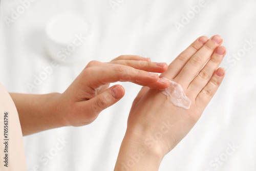 Young woman with dry skin applying cream onto her hand on bed  closeup