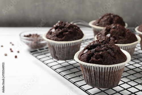 Tasty chocolate muffins and cooling rack on white table  closeup
