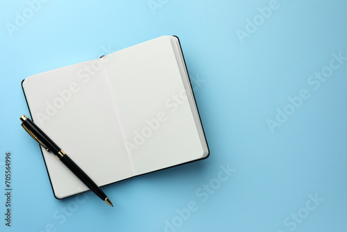 Open notebook with blank pages and pen on light blue background, top view. Space for text photo