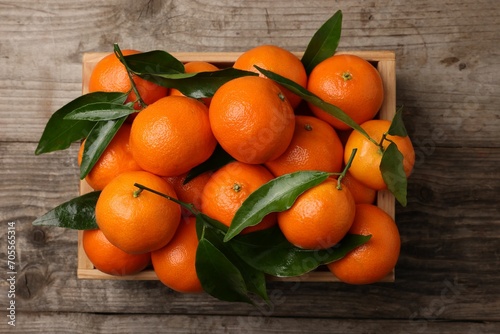 Delicious tangerines with leaves in crate on wooden table, top view