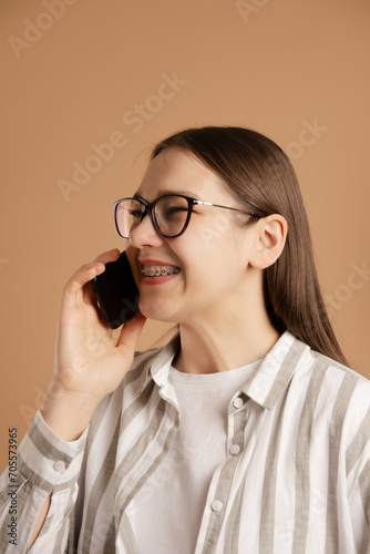 young woman with braces call and talk on smartphone on beige background