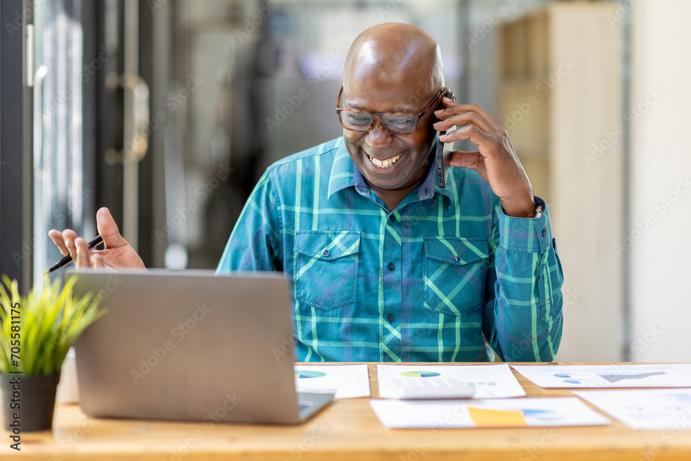 Portrait of Senior African man sitting on laptop at the home office and having a phone conversation with the insurance company. - obrazy, fototapety, plakaty 
