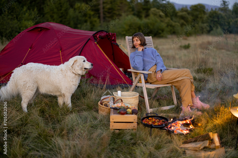Φωτογραφία Woman has a picnic, sitting by the bonfire on wooden chair near tent with her do