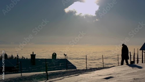 Silhouette eines Paars mit Hund geht im Schnee spazieren, dahinter eine Nebeldecke im grellen Sonnenlicht mit Blick auf die Alpen photo