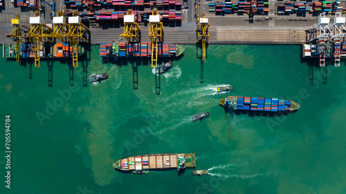 commercial port loading and unloading cargo from container ship import and export by crane for distributing goods by trailers transported to customers and dealers, aerial top view