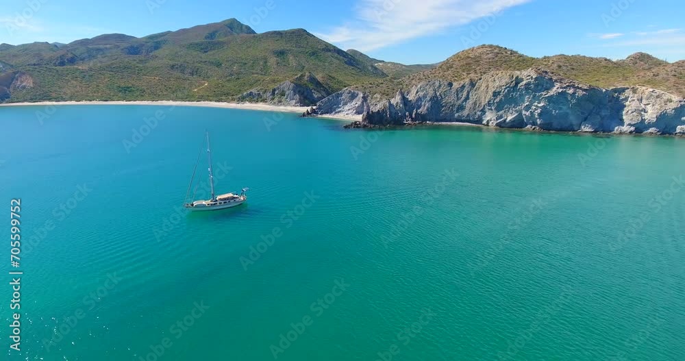 A group of monohull sailing yachts anchored in a brilliantly turquoise blue bay along a pristine beach at the base of small mountainous islands A group of monohull sailing yachts anchored in a brilliantly turquoise blue bay along a pristine beach at the base of small mountainous islands