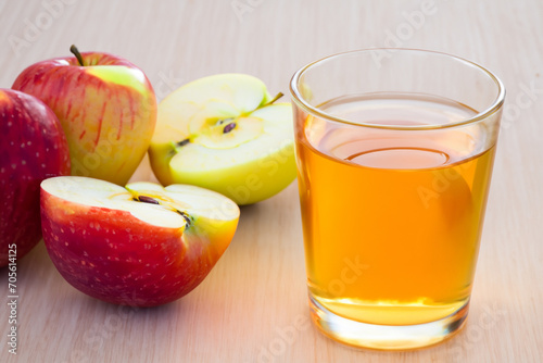Apple juice. on a wooden table there is a transparent glass with apple juice, next to it lies a large number of red apples