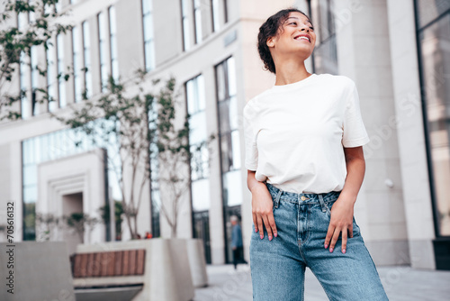 Young beautiful smiling hipster woman in trendy summer white t-shirt and jeans clothes. Carefree woman, posing in the street at sunny day. Positive model outdoors. Cheerful and happy.