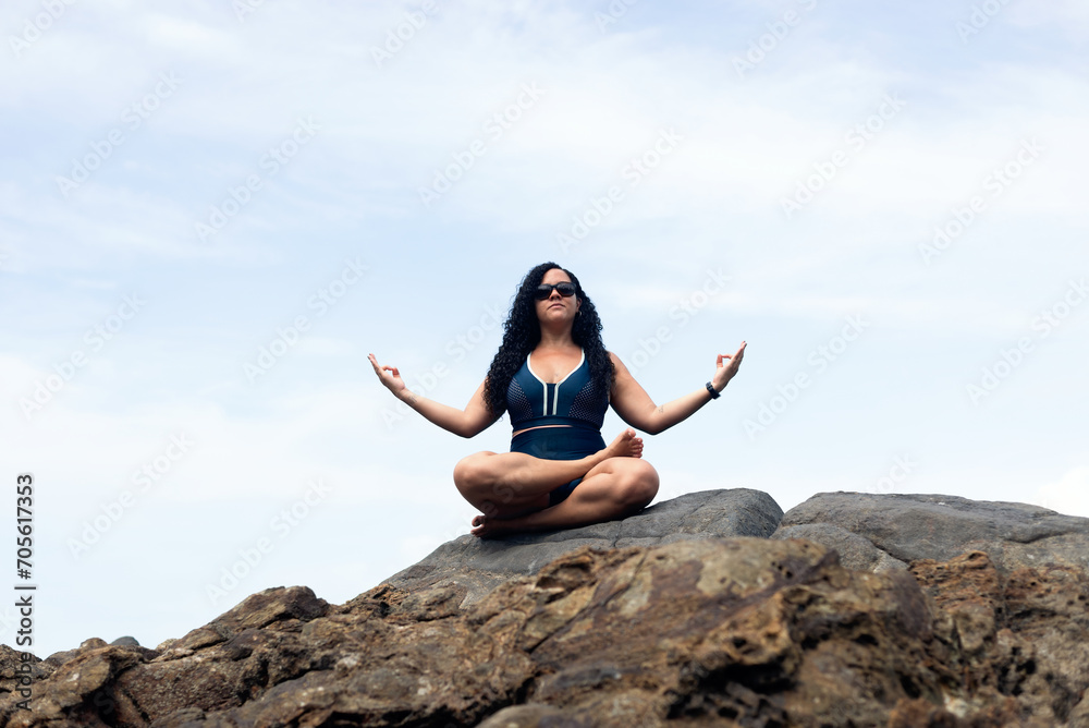 Beautiful, curly-haired woman sitting on the rock of a beach doing yoga exercise. Beautiful, curly-haired woman sitting on the rock of a beach doing yoga exercise.