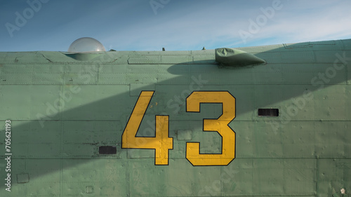 Number 43 written on side of old green aircraft. Metal surface with rivets partially covered with diagonal shadow photo