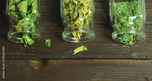 Dry aromatic herbs in glass jars. Wooden table, top view.