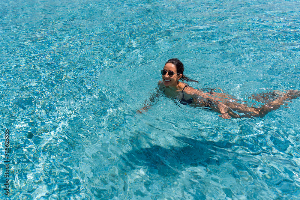 A woman glides through a clear, sparkling blue pool, her arms stretched out as she takes a relaxed swim.