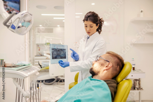 A serious dentist is showing x-ray to a patient at dentist office.