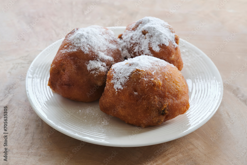 Typical dutch food commonly known as dutch doughnuts, dutchies or oliebollen with currants and powdered sugar on a white plate. Traditionally eaten on new year's eve in the Netherlands.