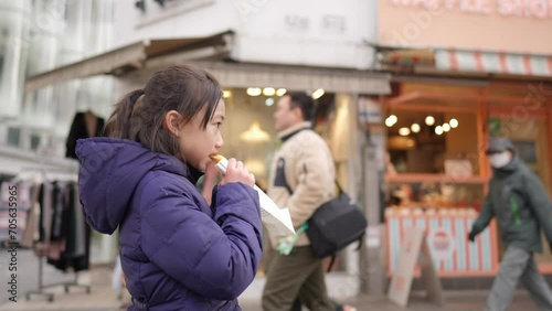 冬の寒い日に韓国のソウルで韓国人の女の子が揚げパンを買って食べているスローモーション映像  Slow motion video of a Korean girl buying and eating fried bread in Seoul, South Korea on a cold winter day photo