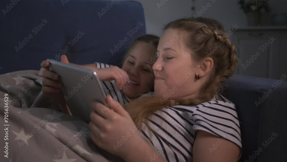 Children watch tablet lying on couch under warm blanket. Children watch movie on digital tablet secretly from adults while they sleep. children secretly play tablet under covers on couc Children watch tablet lying on couch under warm blanket. Children watch movie on digital tablet secretly from adults while they sleep. children secretly play tablet under covers on couc