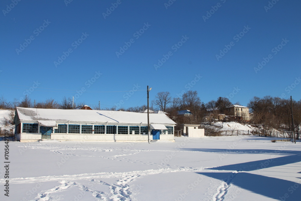 A snowy field with a building and trees in the background