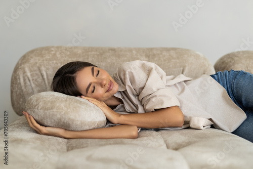 Peaceful woman lying on back on comfortable couch at home, covering eyes with hand, sleeping at daytim photo