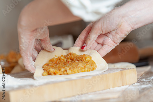 Female hands folding a sheet of dough with filling....