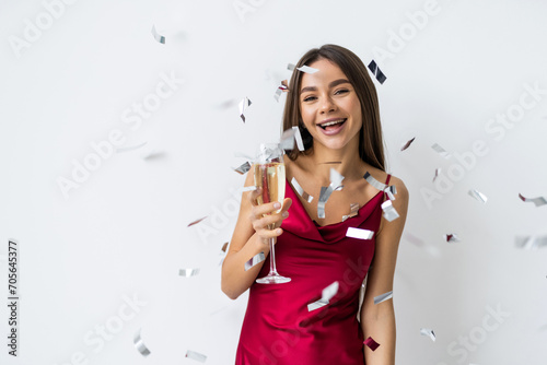 Young woman on white drinking champagne, celebrating new year, wearing dress sparkling confetti, holding glass