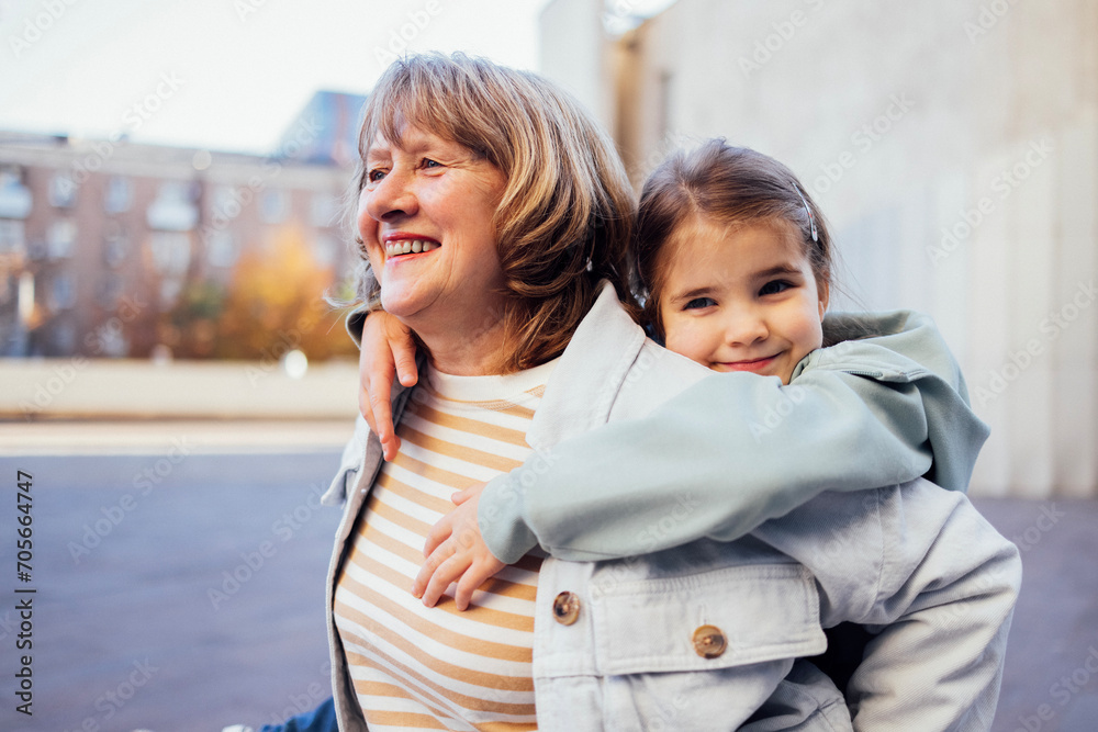 Little girl hugging smiling middle aged woman. Cute female kid and her grandmother enjoy walking outdoors