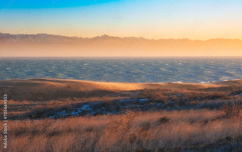 The sea or lake against the backdrop of snowy mountains among the dunes during sunset. Landscape with wind on the Kapchagay reservoir in Kazakhstan Almaty