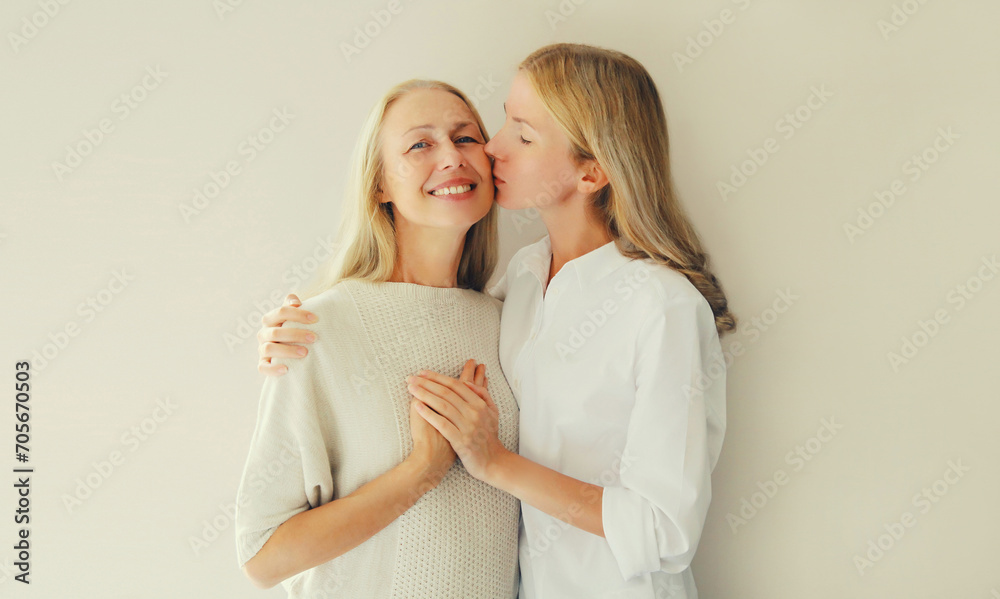 Portrait of adult daughter kissing her happy smiling caucasian middle aged mother on studio background - obrazy, fototapety, plakaty 