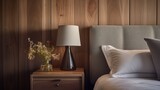 Bedside drawer nightstand and lamp near bed with grey fabric headboard against wood paneling wall