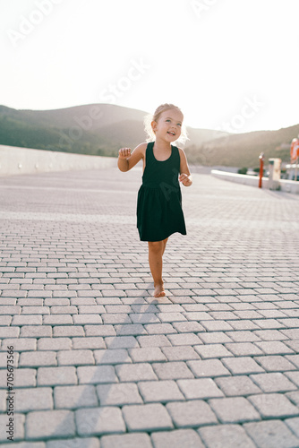 Little laughing girl walks barefoot on a tiled road, dancing and waving her arms