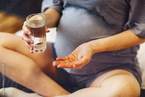 Pregnant woman taking prenatal vitamins during pregnancy, holding water glass and pill in her hands photo